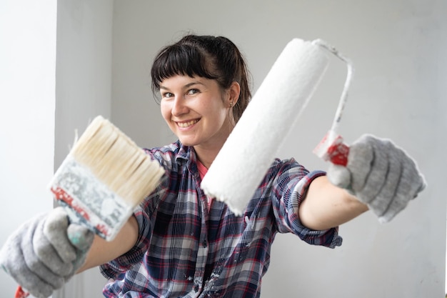 Happy woman in paint roller and white paint for walls in hands closeup portrait Construction work and cosmetic repairs in house wall painting tinting finishing work with your own hands