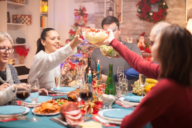 クリスマスの家族の夕食で彼の娘にテーブルの上にサラダを渡す幸せな女性。