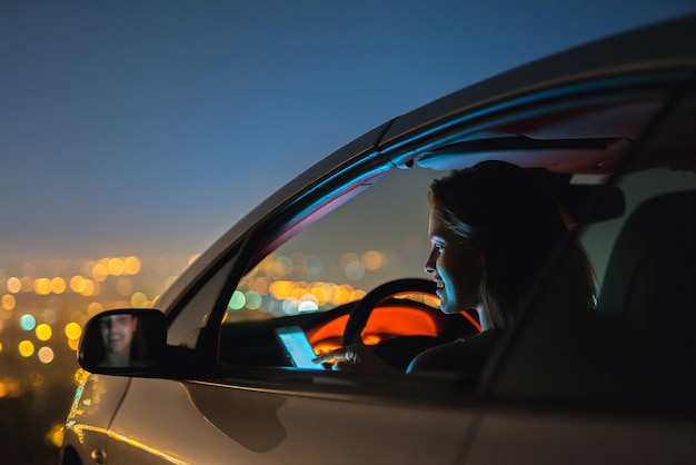 Счастливый телефон женщины в машине на фоне городских огней. вечер ночное время