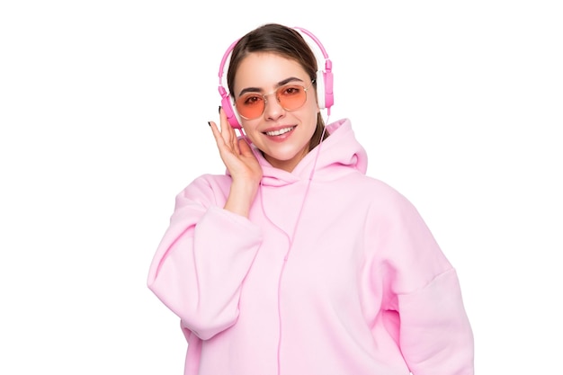 Happy woman in pink hoodie and glasses listening to music in headphones isolated on white