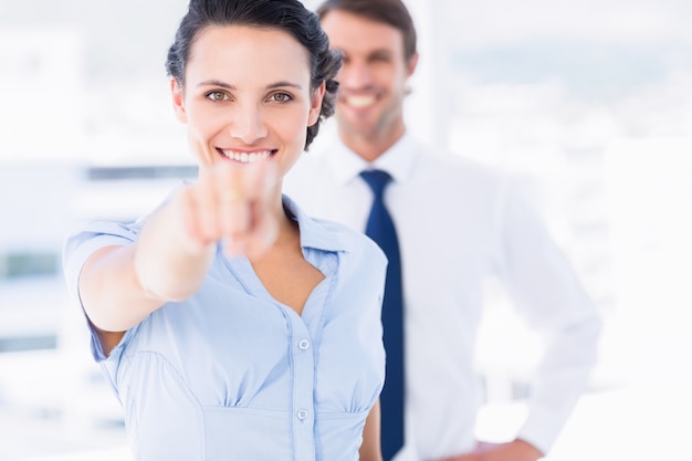 Happy woman pointing at camera with colleague in background