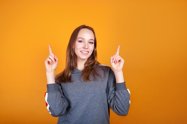 黄色の背景の上のスペースをコピーするために指で指して幸せな女性