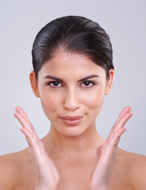 Happy woman portrait and face with skincare cosmetics or facial treatment on a gray studio background Young female person brunette or model with smile in satisfaction for beauty makeup or spa