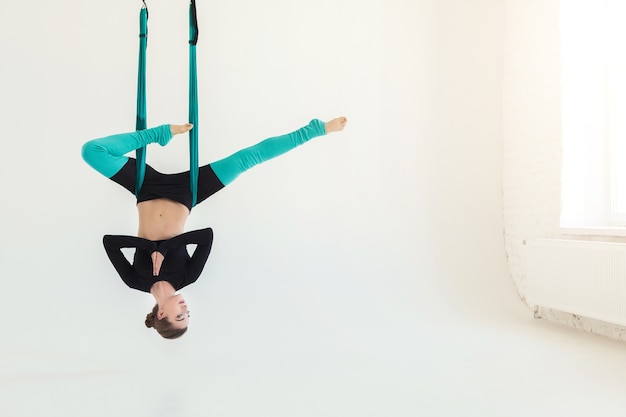 Happy woman practicing fly yoga asana over white background in fitness studio, copy space. Health, sport, yoga concept