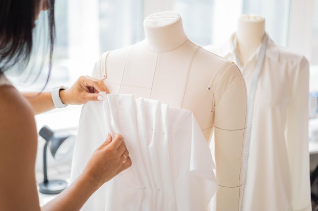 Happy woman professional tailor trying tissue pattern on mannequin working at sewing studio