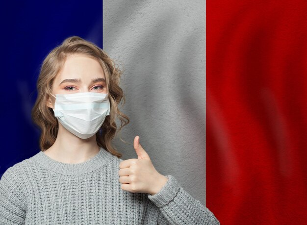 Happy woman in protective mask holding thumb up on national flag France background Flu epidemic and virus protection concept