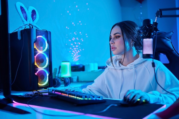 Happy woman putting on headphones and playing computer game Female gamer in glasses sitting and looking at computer monitor