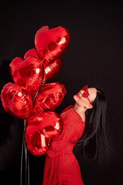 happy woman in a red dress holds a bunch of balls of hearts Valentines Day concept