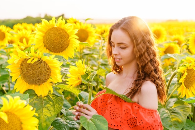 Happy woman in a red dress at sunset in a field of sunflowers smiling sweetly