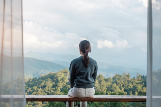 朝の田舎の家やホームステイでリラックスして山の景色を眺める幸せな女性。休暇、ブロガー、SoloTravel、旅、旅行、リラックスのコンセプト