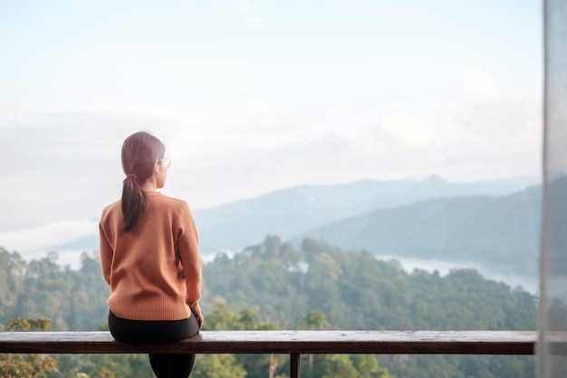 朝の田舎の家やホームステイでリラックスして山の景色を眺める幸せな女性。休暇、ブロガー、SoloTravel、旅、旅行、リラックスのコンセプト