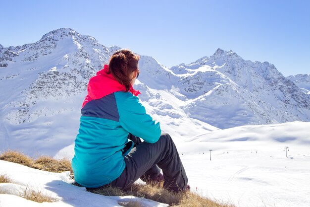 Donna felice che si rilassa sulla cima della montagna sotto il cielo blu con luce solare al giorno di inverno soleggiato, vacanza di viaggio, montagne del paesaggio.