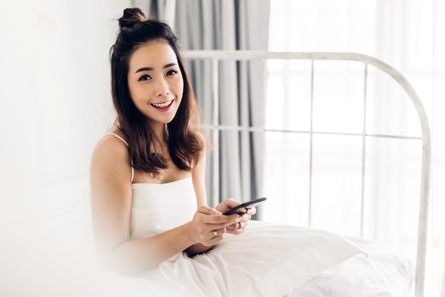 Happy woman relaxing and using smartphone on the bed at home