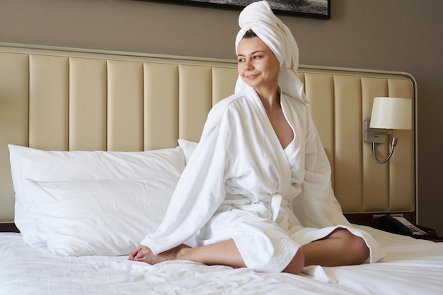 Happy woman resting on the bed after showering at home or in hotel room