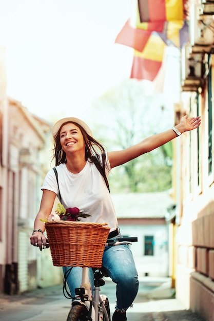 Happy woman riding the bike along the city street, in summer sunny day, smiling of joy during outdoor activity.