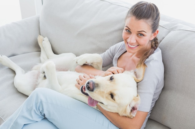 Happy woman rubbing her yellow labrador on the couch