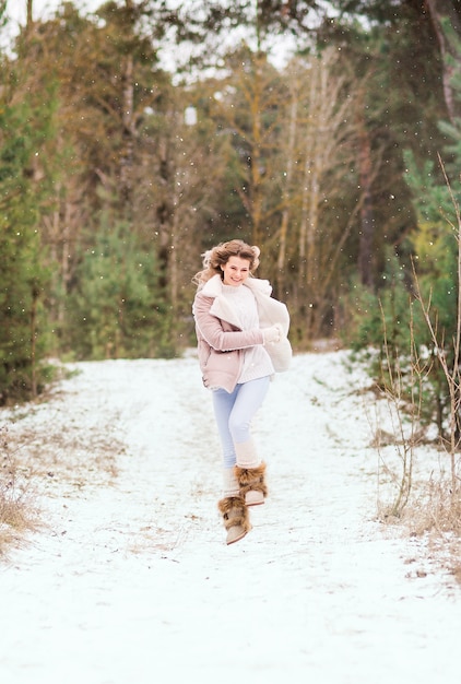 Happy woman runs and jumps in the winter forest. She's wearing light clothes..