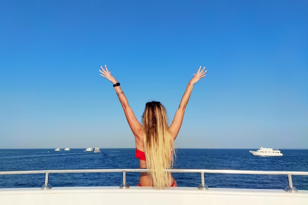 Happy woman on sailboat back side of cheerful girl with raised up hand enjoying majestic seaview summer vacation concept girl spread her arms out to the sides feeling effect of flying in motion