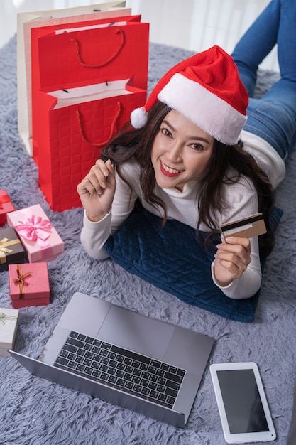 Donna felice in cappello della santa che compera online per il regalo di natale con il computer portatile in salone