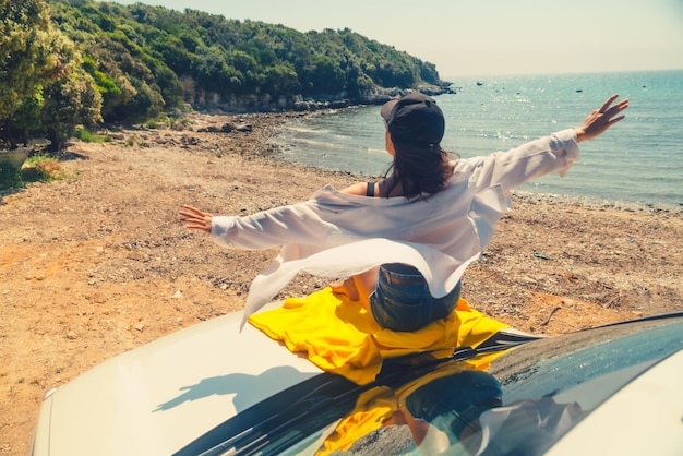 Happy woman at sea summer beach sitting at car hood