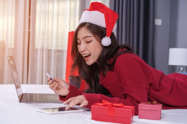 Happy woman shopping online for Christmas gift with digital tablet and credit card on bed