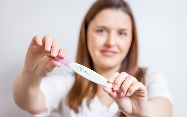 Happy woman showing her positive result on the pregnancy test over a white background