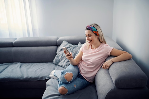 A happy woman sits on the sofa in living room and texting messages on the phone