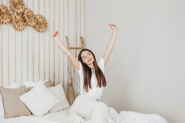 Donna felice seduta sul letto che si allunga dopo il sonno e sorride nella sua stanza