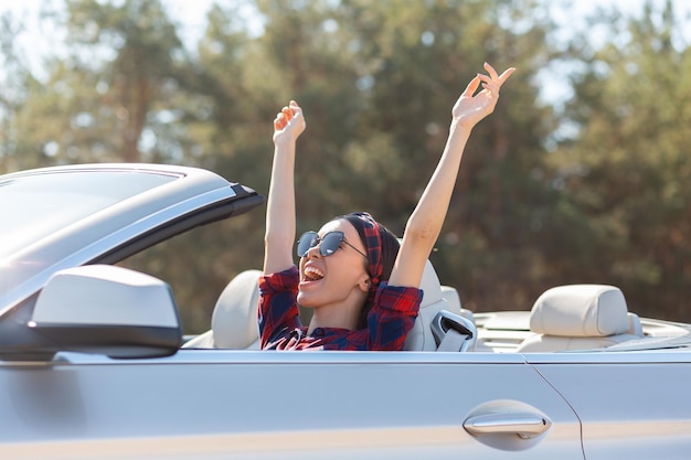 Happy woman sitting in the car and holding hands up