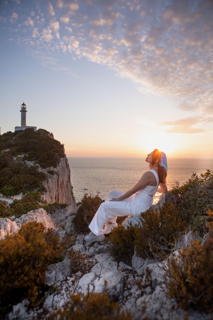 Happy woman sitting at the cliff view view of Lefkada island lighthouse