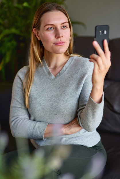 ラップトップとソファに座って、自宅で電話で話している幸せな女性。