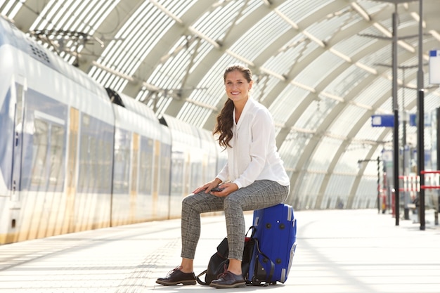 Happy woman sitting on suitcase holding smart phone