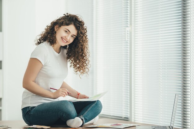 La donna felice seduta sul tavolo e che disegna sulla carta