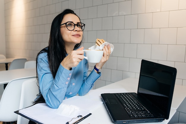 Happy woman sitting at table and drinking coffee with sandwich