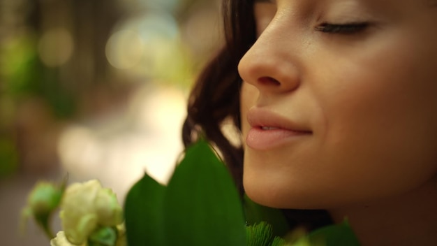 Happy woman smelling flowers in park Closeup romantic girl holding rose bouquet outdoors Portrait of gorgeous bride putting roses close to face in garden