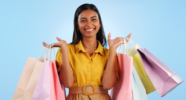 Photo happy woman smile and hand with shopping bags in studio for mock up in retail marketing or promotion on blue background indian person shopaholic and portrait in offer in fashion cosmetic or sale