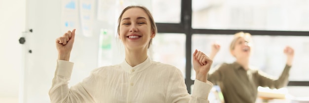 La donna felice sorride alzando le mani alla fine della giornata lavorativa. i colleghi si siedono ai tavoli in un ambiente moderno