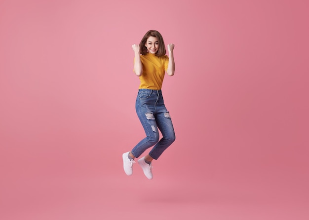 행복 한 여자 는 분홍색 배경 에 고립 되어 성공 을 축하 하는 동안 미소 짓고 점프 한다