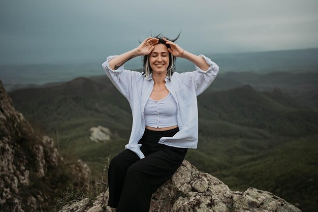 Happy woman smiling tourist hiking up mountain enjoying nature landscape in cloudy gloomy windy