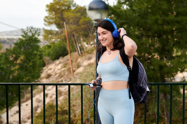 Happy woman in sportswear listens to music outdoors
