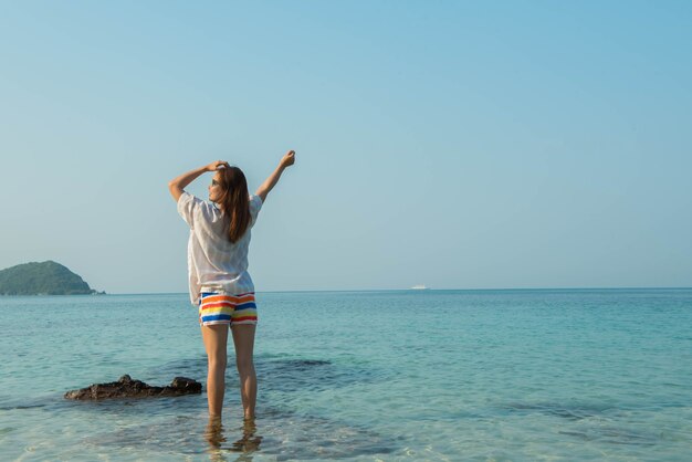 海のビーチで腕を伸ばして立っている幸せな女性