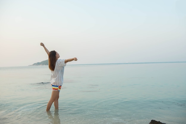 腕を伸ばして立っている幸せな女性と海のビーチでの生活をお楽しみください