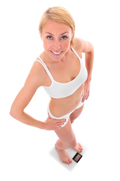 a happy woman standing on a bathroom scales over white