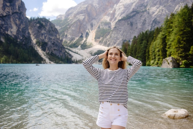 Happy woman standing by the mountain lake and enjoying the beautiful scenery on a sunny day