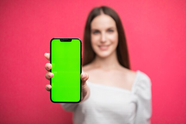 Happy woman standing and hold smartphone on pink background. Green screen phone screen