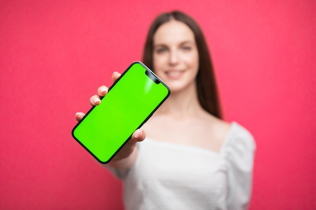 분홍색 배경에 스마트폰을 들고 서 있는 행복한 여자. 녹색 화면 전화 화면