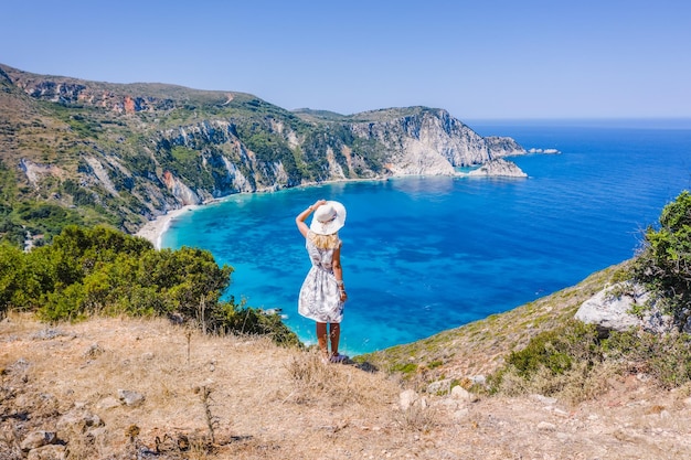 Happy woman standing on top of a rock with hat enjoying Myrtos Beach Cephalonia island Greece