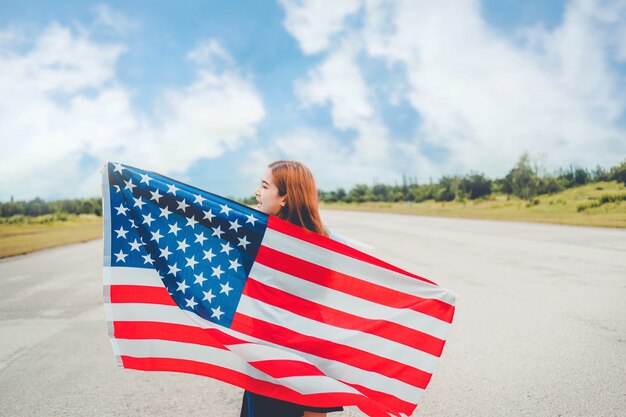 アメリカの国旗と一緒に立っている幸せな女性愛国心の休日。米国は7月4日を祝う