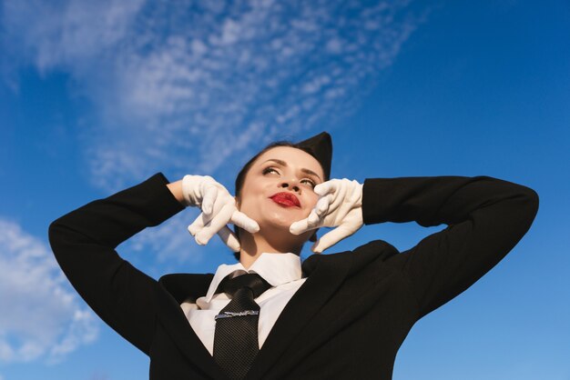 空の背景にカメラでポーズをとって制服の幸せな女性スチュワーデス