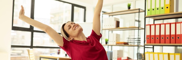 Photo happy woman stretches back and arms after finishing report in office relaxed female employee